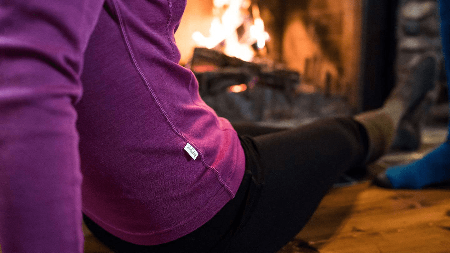 woman sitting by fireplace while wearing minus33 merino wool midweight base layer shirt and long john underwear bottoms