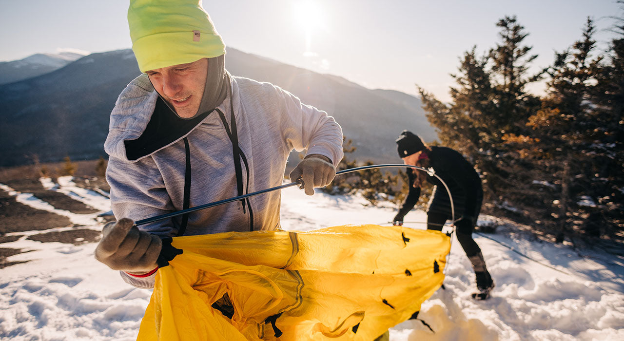 man setting up tent on top of snowy mountain wearing expedition kodiak fleece hoodie