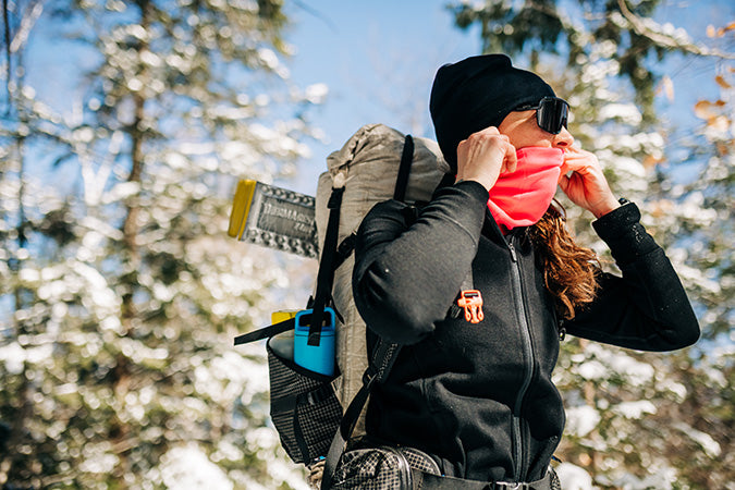 woman hiking wearing midweight ridge cuff beanie and midweight blaze pink neck gaiter