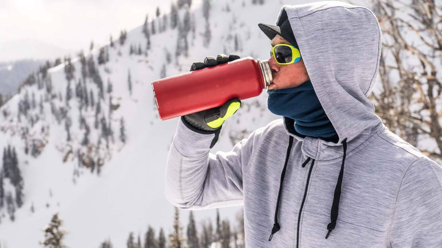 man drinking water in the snow while wearing minus33 merino wool expedition weight hoodie sweatshirt
