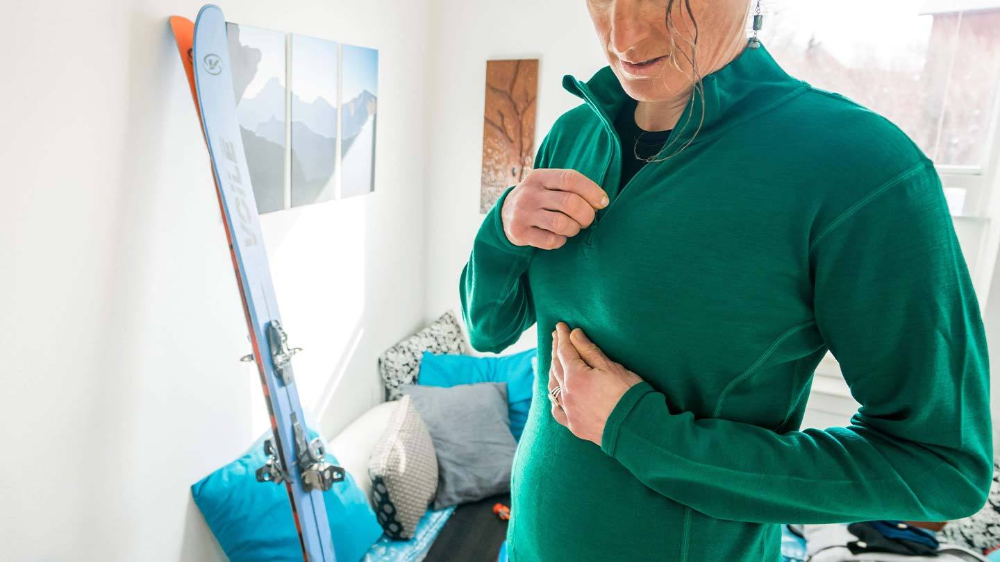 woman getting ready to go skiing while zipping up minus33 merino wool midweight 1/4 zip shirt mid layer