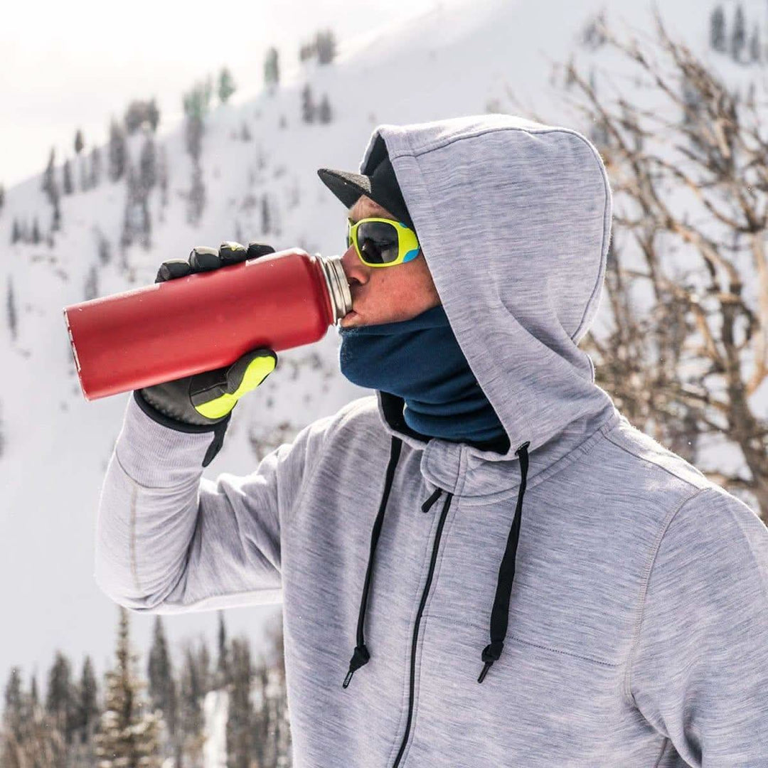 A man stops on his winter hike to take a sip from his thermos. The heavyweight brushed wool Kodiak Fleece Hoodie, crafted with thumbholes and a drawstring to bundle you up for wicked cold days! #color_ash-gray