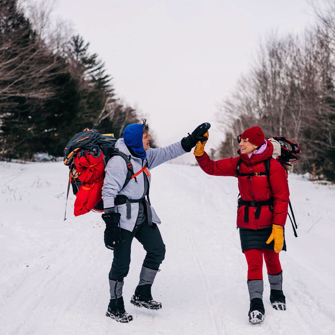 A man and a woman walk down the snowy mountain. The man is modeling the heavyweight brushed wool Kodiak Fleece Hoodie, crafted with thumbholes and a drawstring to bundle you up for wicked cold days! #color_ash-gray