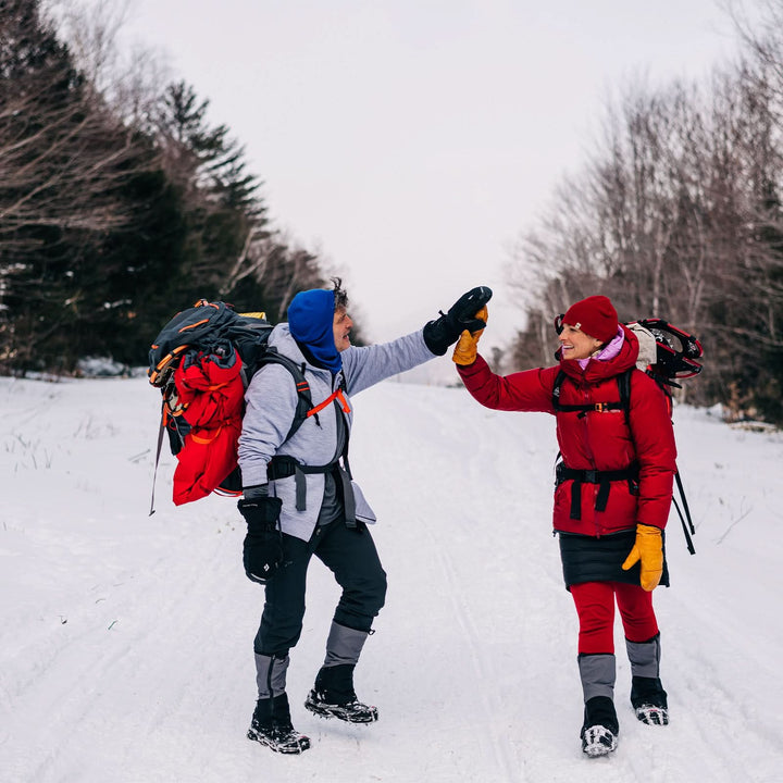 A man and a woman walk down the snowy mountain. The man is modeling the heavyweight brushed wool Kodiak Fleece Hoodie, crafted with thumbholes and a drawstring to bundle you up for wicked cold days! #color_ash-gray
