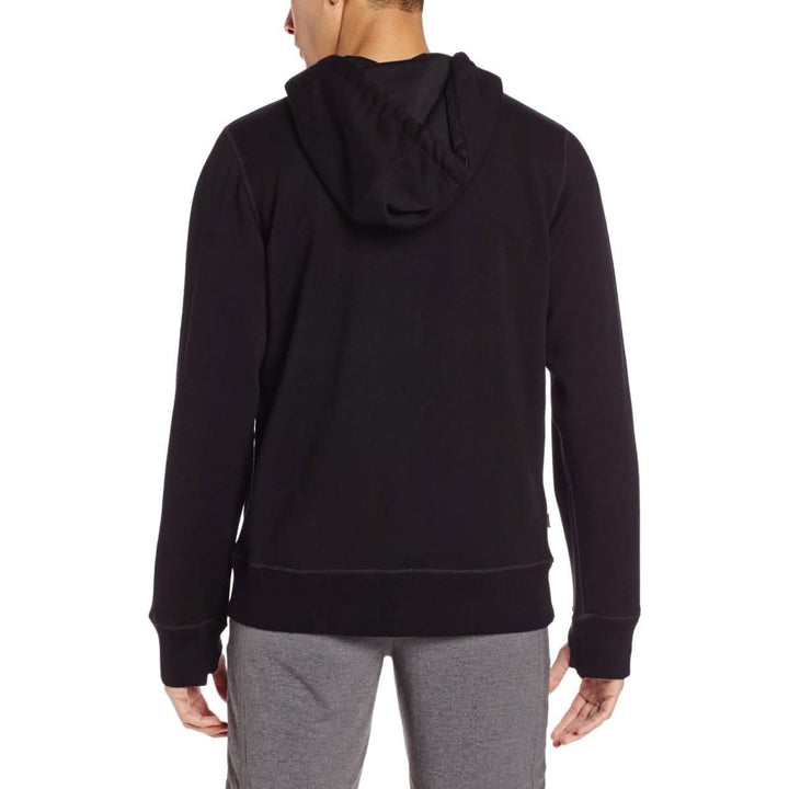A man models the heavyweight brushed wool Kodiak Fleece Hoodie, crafted with thumbholes and a drawstring to bundle you up for wicked cold days! #color_black
