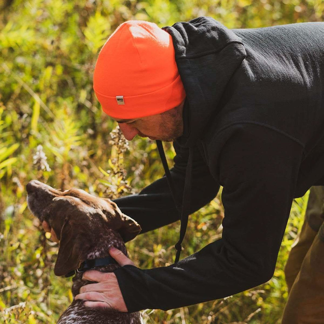 A man pets his hunting dog while wearing the heavyweight brushed wool Kodiak Fleece Hoodie, crafted with thumbholes and a drawstring to bundle you up for wicked cold days! #color_black