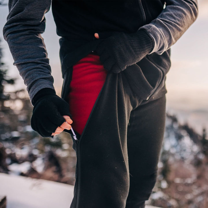 man out in the snow zipping up his zip off bottoms that are heavyweight and 100% merino wool