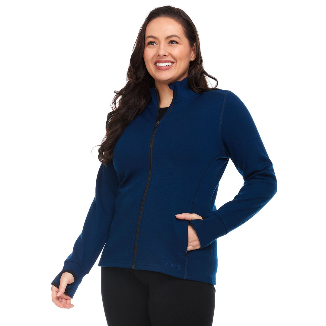 A woman models a hundred percent merino wool heavyweight full zip sweater. This outer layer features a two and a half inch mock neck collar, two zippered pockets, and thumbholes. #color_navy