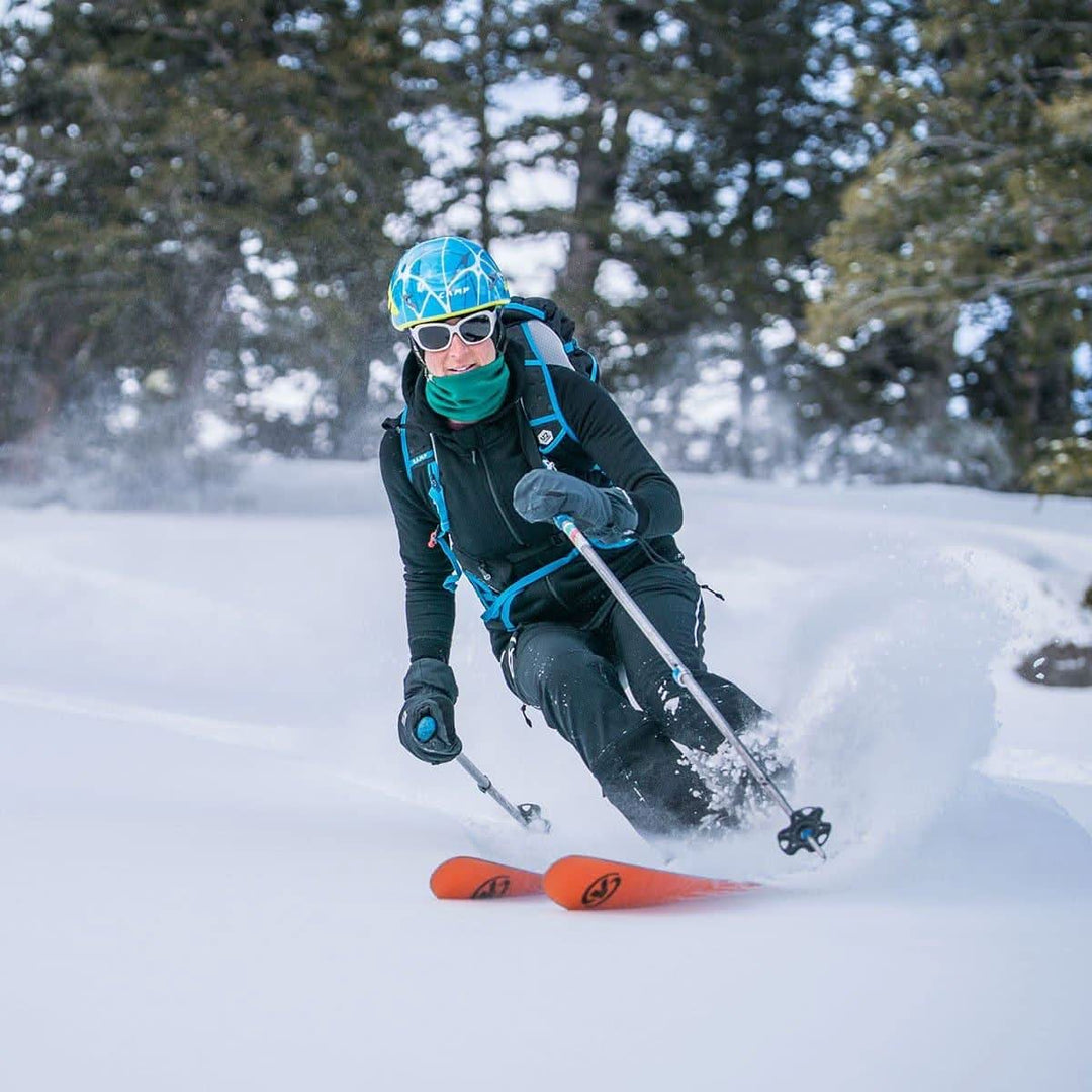 A woman models the heavyweight merino wool brushed fleece hoodie while skiing the slopes. The hoodie features a large hood with drawstrings, thumbholes, two pockets, and an interior stash pocket inside. #color_black