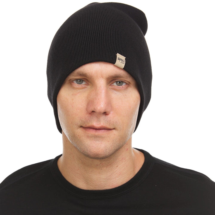 A man models a heavyweight, super soft, one hundred percent merino wool beanie. This heavyweight beanie is the warmest hat that we offer, perfect for hiking through the White Mountains, or sitting at a bonfire in January. #color_black