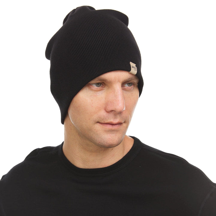A man models a heavyweight, super soft, one hundred percent merino wool beanie. This heavyweight beanie is the warmest hat that we offer, perfect for hiking through the White Mountains, or sitting at a bonfire in January. #color_black