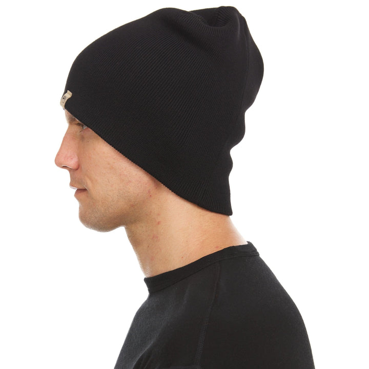 A man models a heavyweight, super soft, one hundred percent merino wool beanie. This heavyweight beanie is the warmest hat that we offer, perfect for hiking through the White Mountains, or sitting at a bonfire in January. #color_black