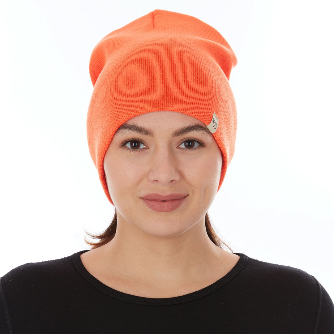 A woman models a heavyweight, super soft, one hundred percent merino wool beanie. This heavyweight beanie is the warmest hat that we offer, perfect for hiking through the White Mountains, or sitting at a bonfire in January. #color_blaze-orange