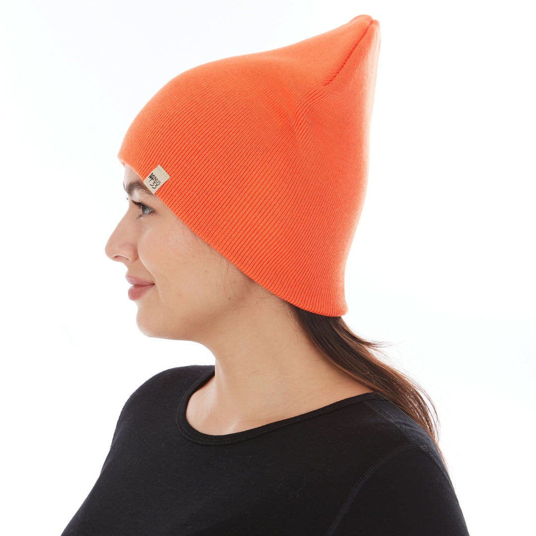 A woman models a heavyweight, super soft, one hundred percent merino wool beanie. This heavyweight beanie is the warmest hat that we offer, perfect for hiking through the White Mountains, or sitting at a bonfire in January. #color_blaze-orange