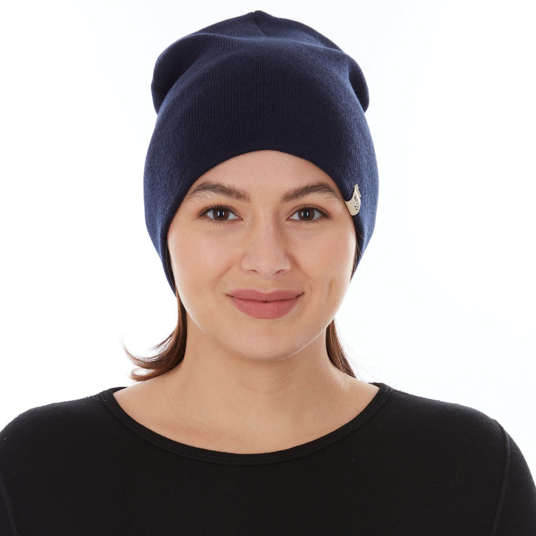 A woman models a heavyweight, super soft, one hundred percent merino wool beanie. This heavyweight beanie is the warmest hat that we offer, perfect for hiking through the White Mountains, or sitting at a bonfire in January. #color_navy