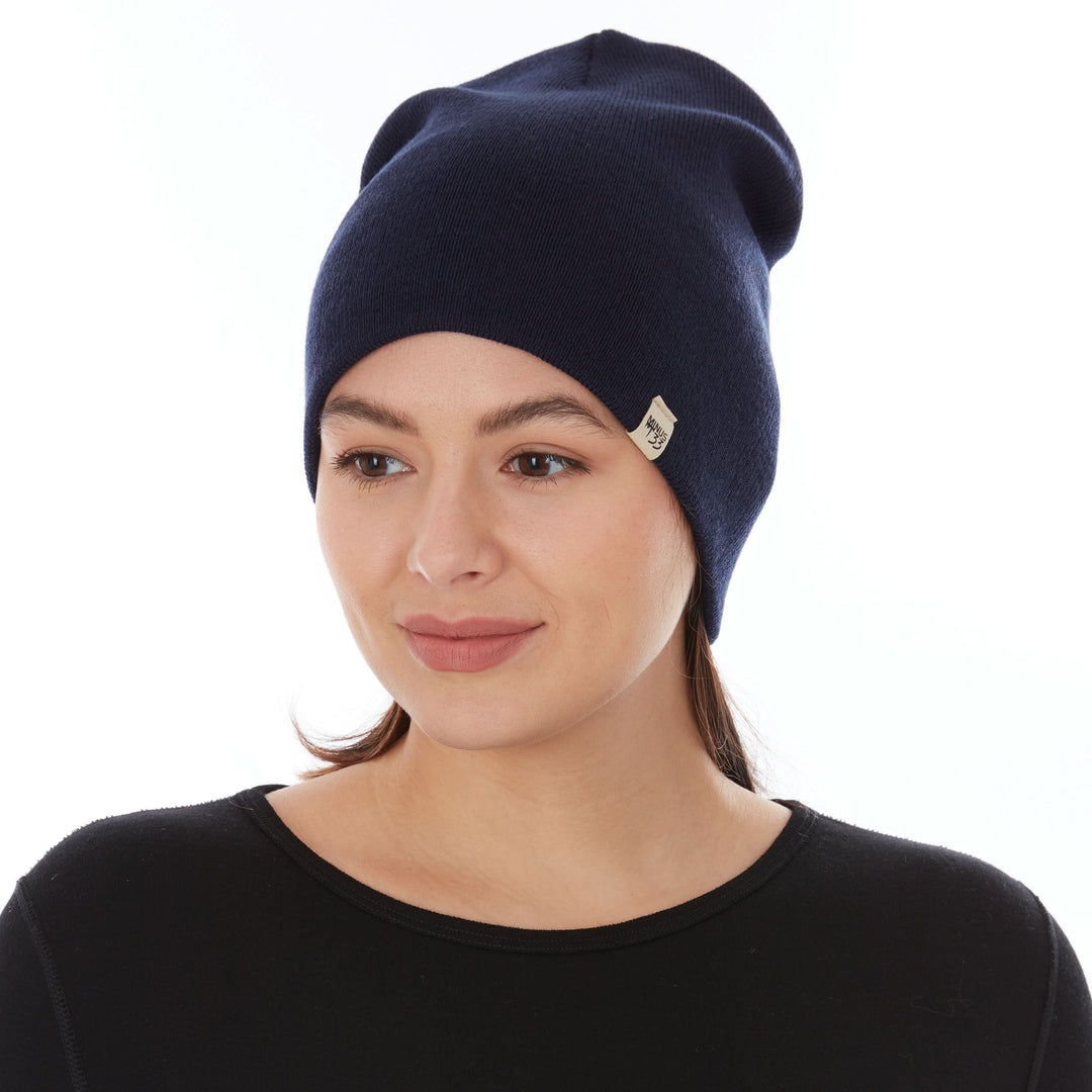 A woman models a heavyweight, super soft, one hundred percent merino wool beanie. This heavyweight beanie is the warmest hat that we offer, perfect for hiking through the White Mountains, or sitting at a bonfire in January. #color_navy