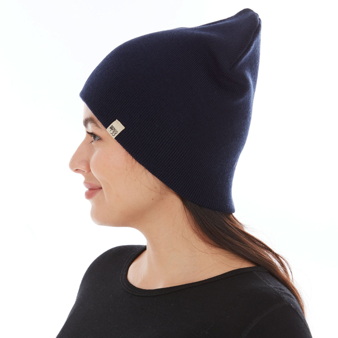 A woman models a heavyweight, super soft, one hundred percent merino wool beanie. This heavyweight beanie is the warmest hat that we offer, perfect for hiking through the White Mountains, or sitting at a bonfire in January. #color_navy