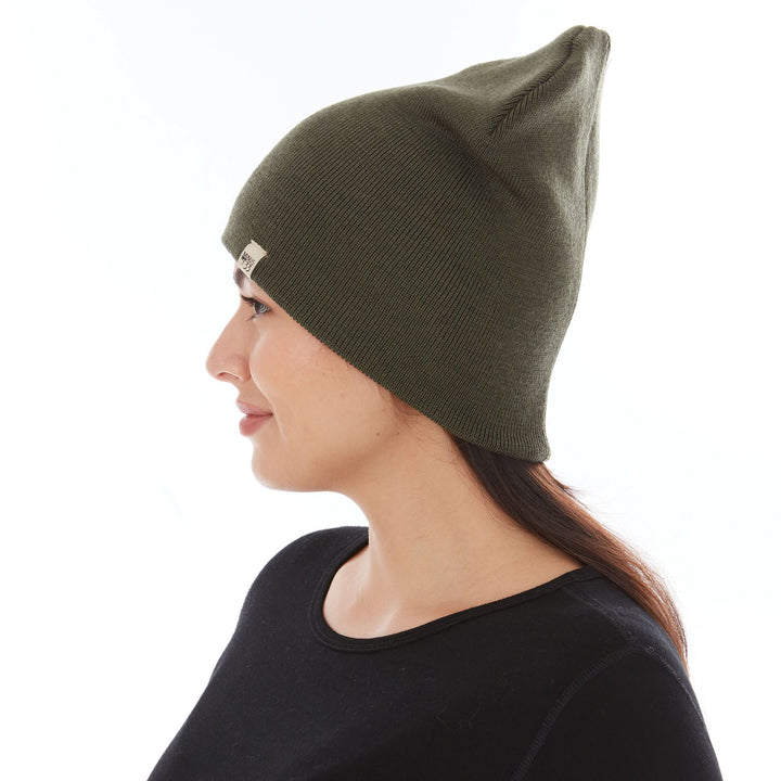 A woman models a heavyweight, super soft, one hundred percent merino wool beanie. This heavyweight beanie is the warmest hat that we offer, perfect for hiking through the White Mountains, or sitting at a bonfire in January. #color_olive-drab-green
