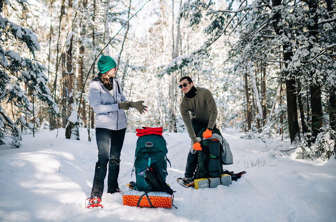 man and woman hiking in the woods in the winter wearing expedition weight and midweight merino wool base layers