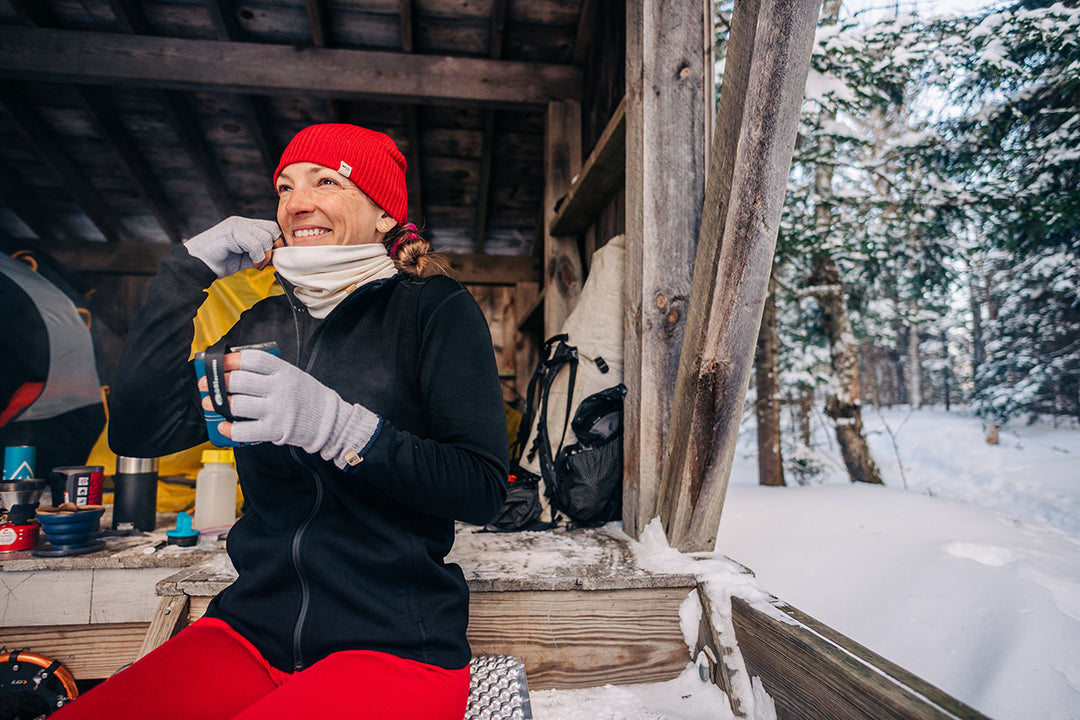 woman winter hiking sitting down drinking coffee while wearing merino wool base layers