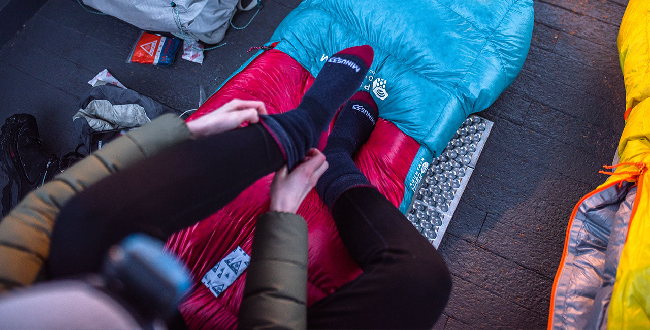 woman sitting on sleeping bag pulling her mountain heritage patriot socks up wearing midweight base layer bottoms