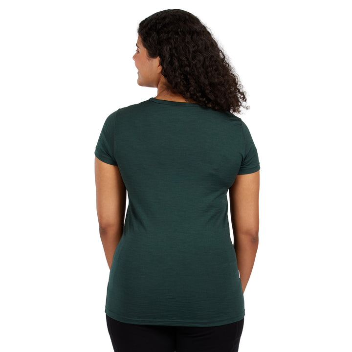A woman with curly dark hair is shown from the back wearing a dark green short-sleeve crewneck t-shirt and black pants, photographed against a solid white background. 