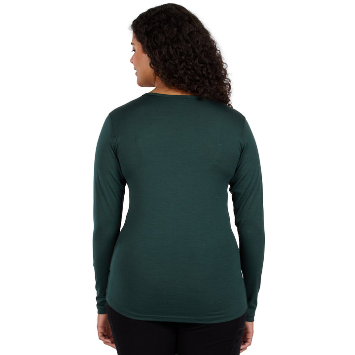 A woman with curly dark hair is shown from the back wearing a dark green 100% merino wool long-sleeve crewneck shirt and black pants against a plain white background. 