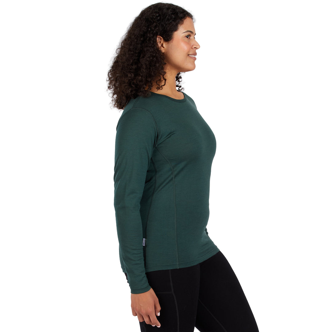 A woman with curly dark hair is shown in profile wearing a dark green long-sleeve 100% Merino wool athletic top and black leggings against a plain white background. 