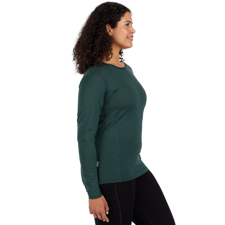 A woman with curly dark hair is shown in profile wearing a dark green long-sleeve 100% Merino wool athletic top and black leggings against a plain white background. 