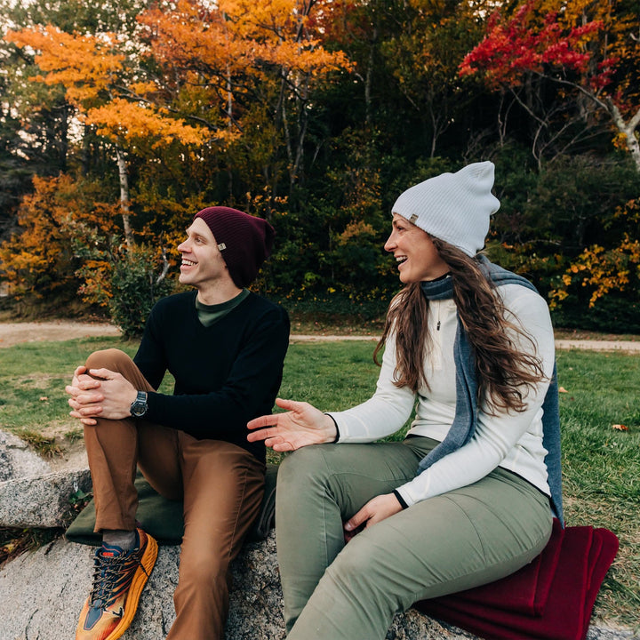 A couple sits on wool blankets to chat. The woman is wearing a one hundred percent merino wool quarter zip sweater 