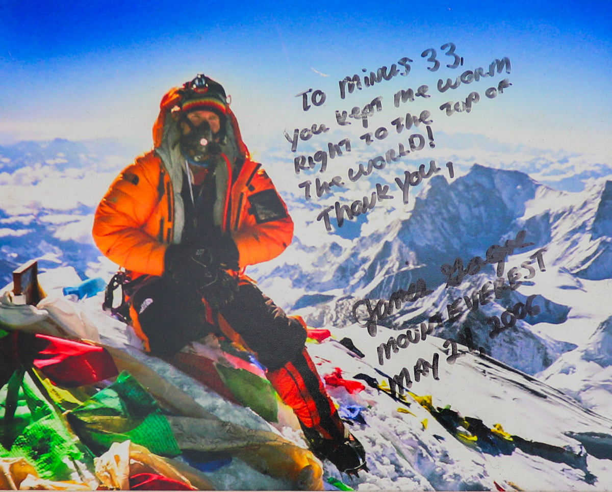 Person in an orange jacket standing on a snow-covered mountain summit with handwritten text over the scene.