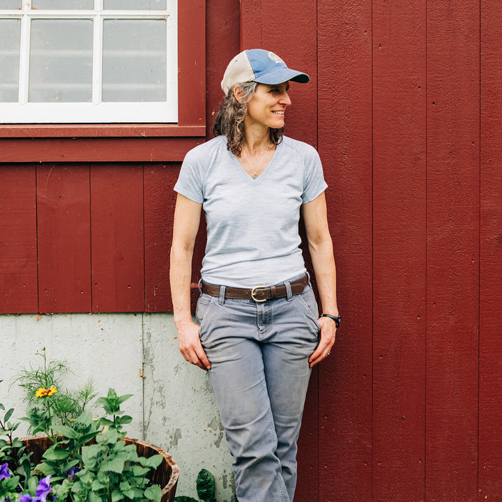 Woman wearing microweight merino wool v-neck stands against barn #color_ash-gray