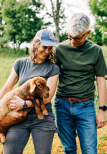 couple in lightweight merino wool t shirts holding a small lamb