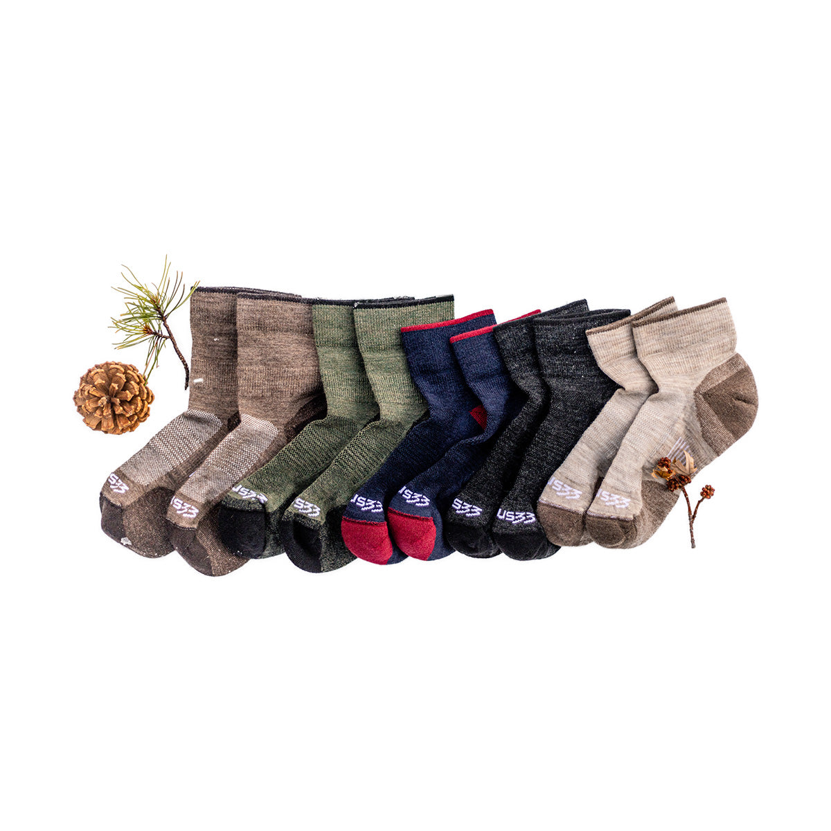 Six pairs of crew socks in brown, green, navy, charcoal, and tan arranged with pinecones and dried foliage on a white background.