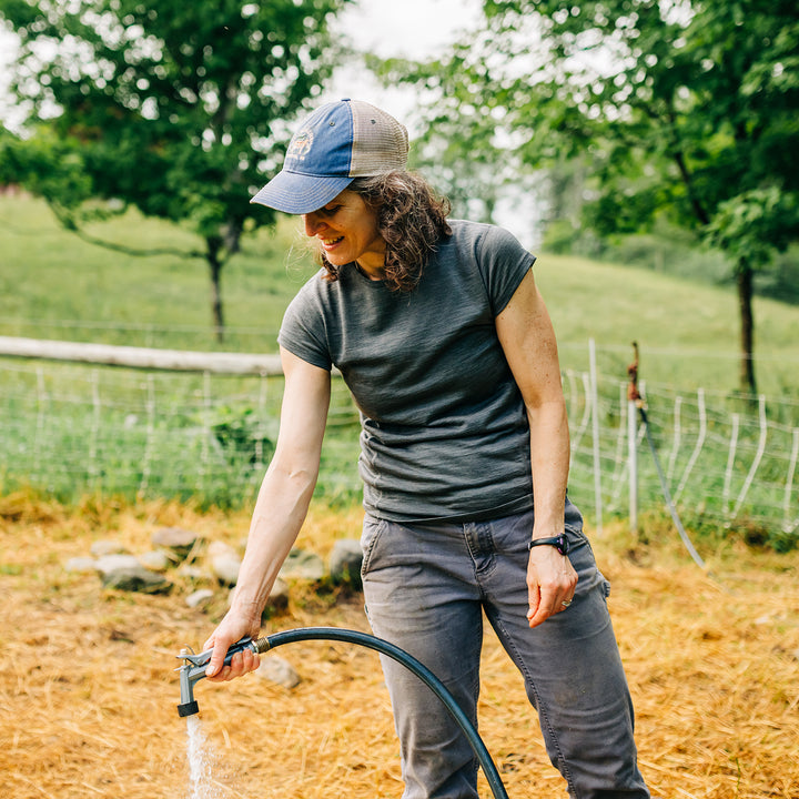 Woman wearing merino wool short sleeve shirt fills water bucket #color_charcoal-gray