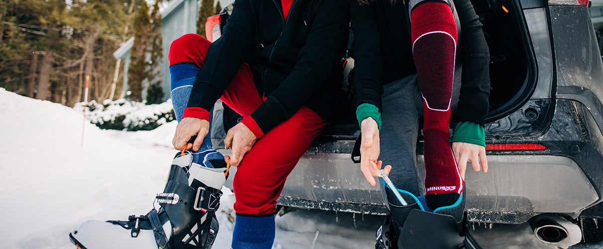 people sitting on a car putting on their ski and snowboard boots wearing usa new hampshire made mountain heritage elite socks
