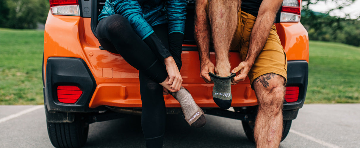 Two people wearing merino wool socks sitting on a bumper