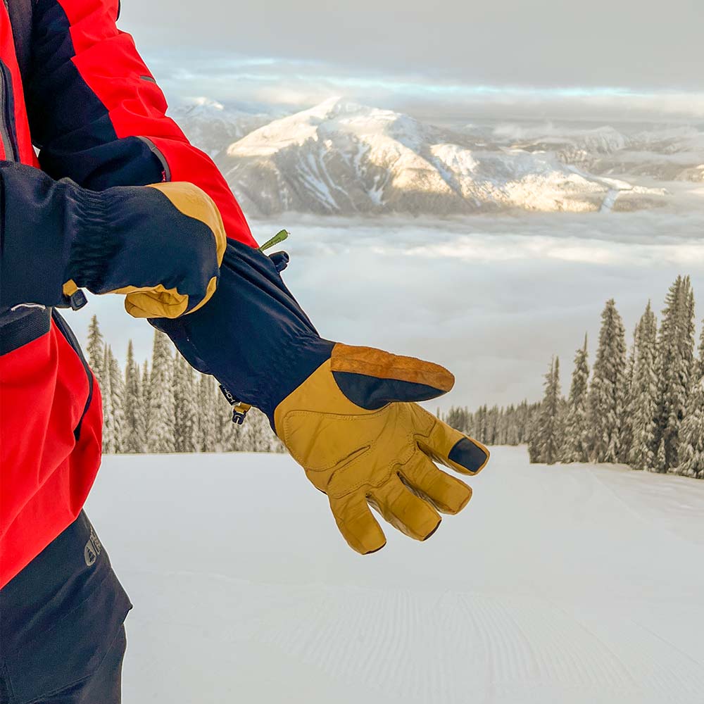 Person wearing tan waterproof ski gloves with a snowy mountain landscape in the background 