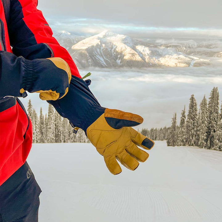 Person wearing tan waterproof ski gloves with a snowy mountain landscape in the background 