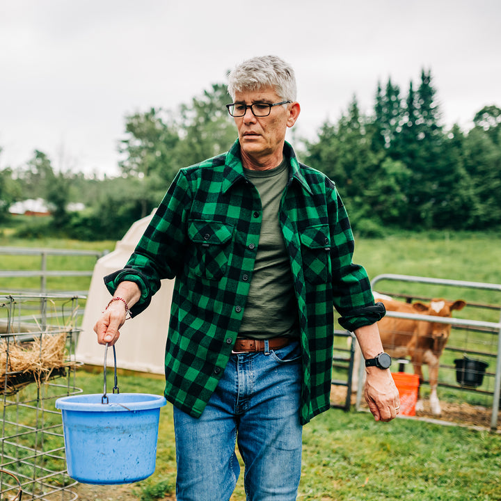 Man wearing green plaid heavyweight wool shirt brings water to dairy calves #color_green-plaid